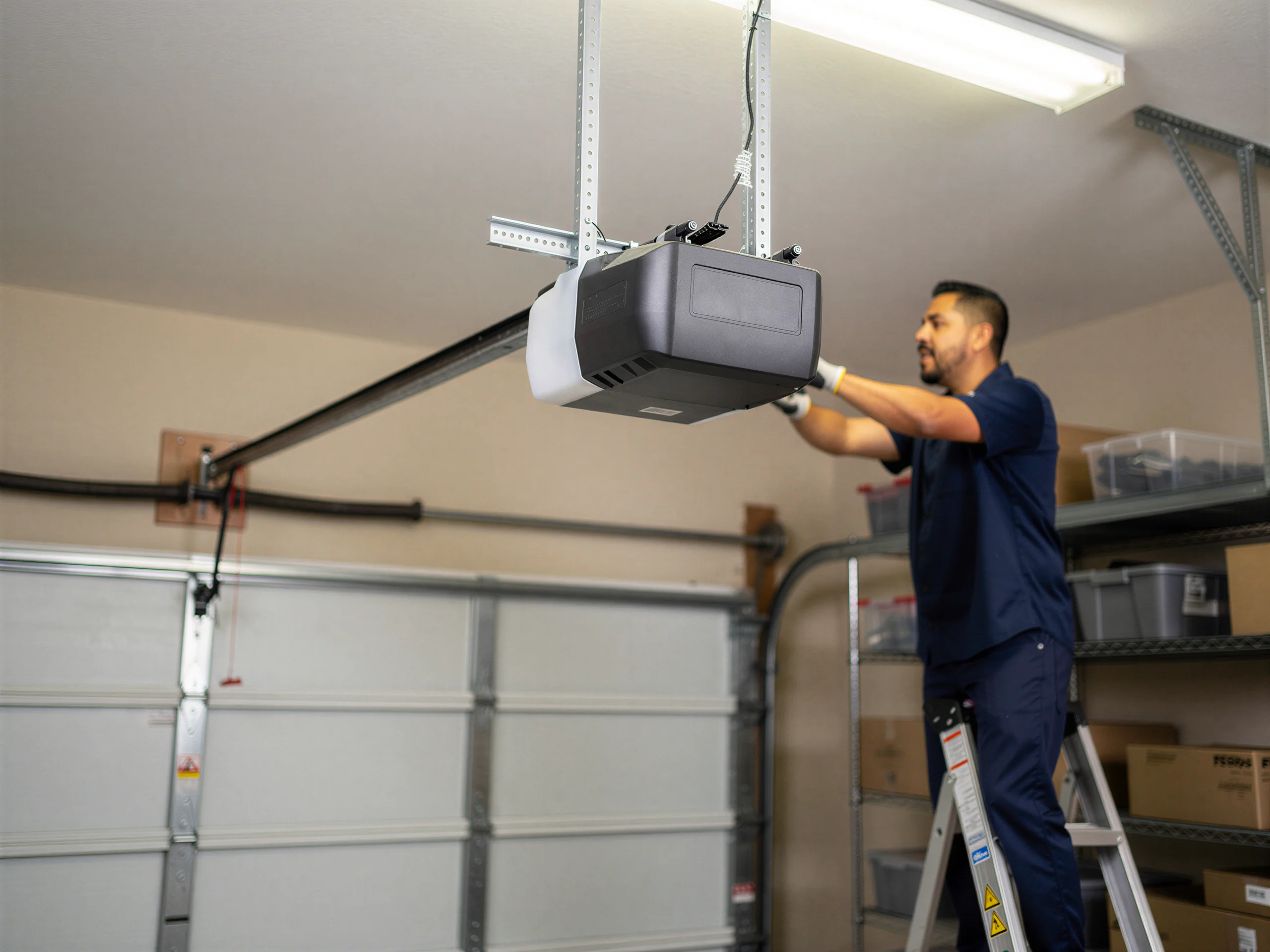 A technician on a ladder installs a garage door opener.